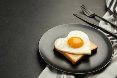 Tasty fried egg in shape of heart with toast served on dark grey table. Space for text
