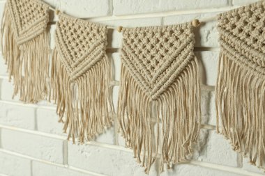Stylish macrame hanging on white brick wall, closeup