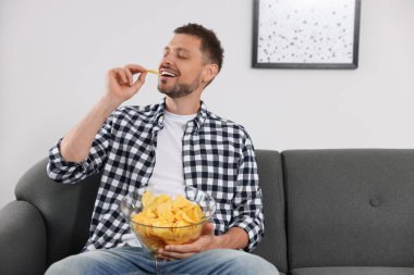 Handsome man eating potato chips on sofa at home