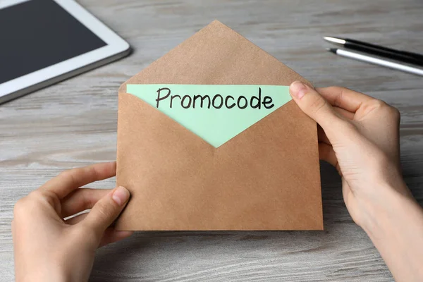 Woman Holding Envelope Card Words Promo Code Wooden Table Closeup — Stock Photo, Image