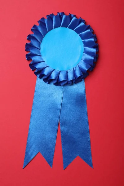 Blue award ribbon on red background, top view