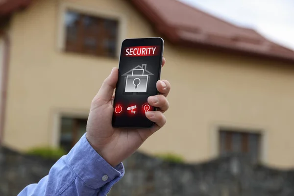 Man using home security application on smartphone in front of house outdoors, closeup