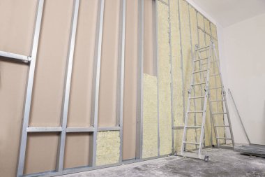 Ladder near wall with metal studs and insulation material indoors
