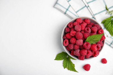 Bowl with fresh ripe raspberries and green leaves on white table, flat lay. Space for text