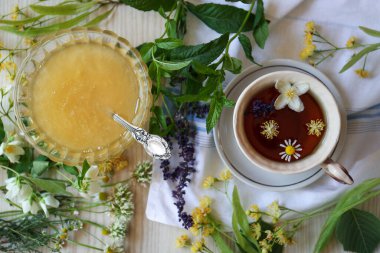 Cup of hot aromatic tea, honey and different fresh herbs on white wooden table, flat lay