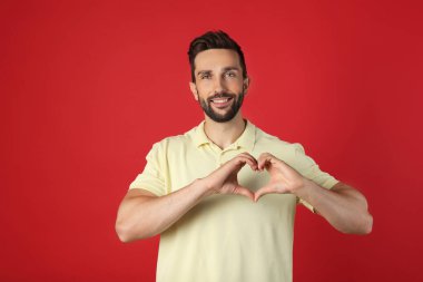 Happy man making heart with hands on red background