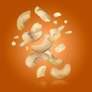 Tasty cashew nuts flying on orange background