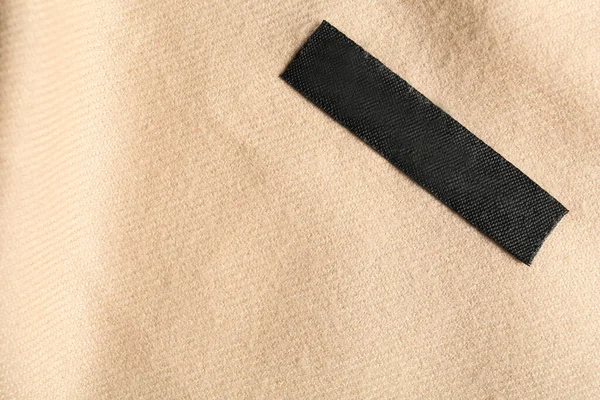 Blank clothing label on beige cashmere apparel, top view. Space for text