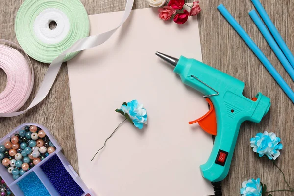 Hot glue gun and handicraft materials on wooden table, flat lay