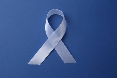 White awareness ribbon on blue background, top view