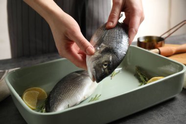 Bir kadın yemek kabına dorada balığı koyuyor, yakın plan.