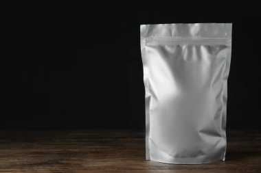 One blank foil package on wooden table against dark background. Space for text