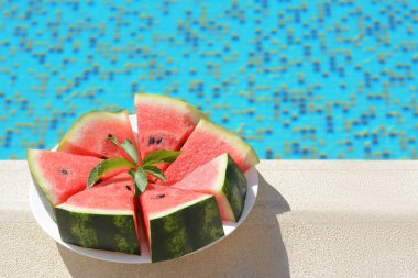 Slices of watermelon on white plate near swimming pool outdoors. Space for text