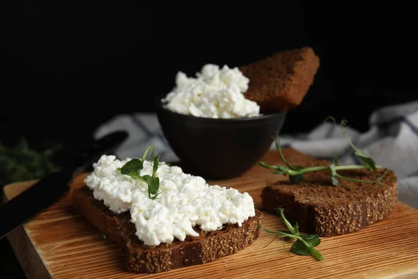Bread with cottage cheese and microgreens on wooden board, closeup
