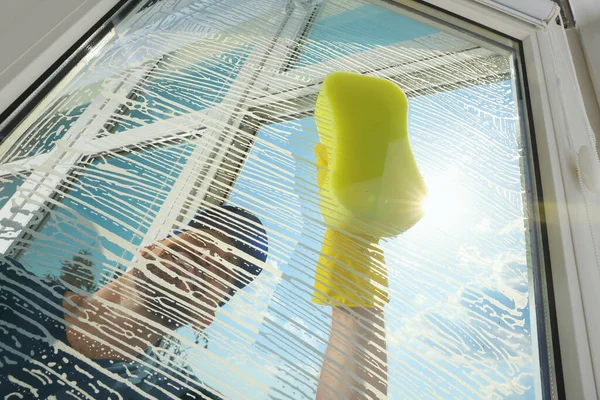 Man cleaning glass with sponge indoors, low angle view