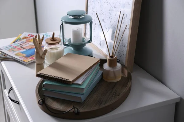 Wooden tray with notebooks, air reed freshener and decor on chest of drawers indoors