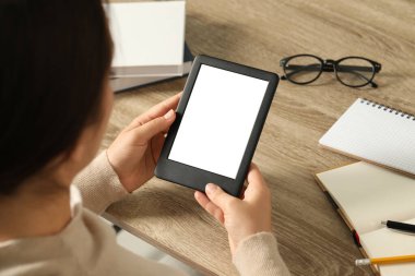Young woman using e-book reader at wooden table, closeup