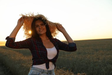 Beautiful young woman in straw hat among ripe wheat field on sunny day, space for text