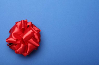 Red ribbon bow on blue background, top view. Space for text