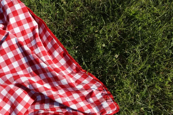 Checkered picnic tablecloth on fresh green grass, top view. Space for text