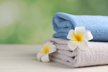Closeup view of soft folded towels and plumeria flowers on white wooden table, space for text