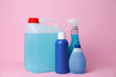 Many bottles of different detergents on pink background. Cleaning supplies