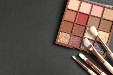 Colorful eyeshadow palette with brushes on dark background, flat lay. Space for text