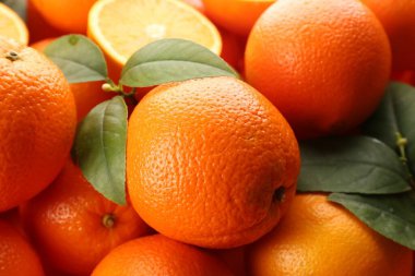 Fresh ripe oranges with green leaves as background, closeup