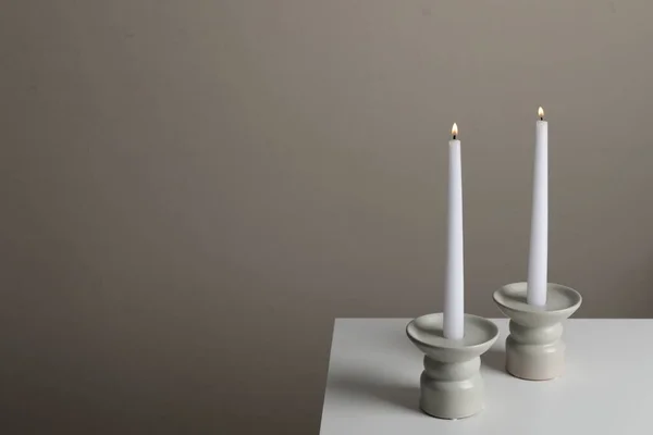 Halter Mit Brennenden Kerzen Auf Weißem Tisch Neben Blassbrauner Wand — Stockfoto