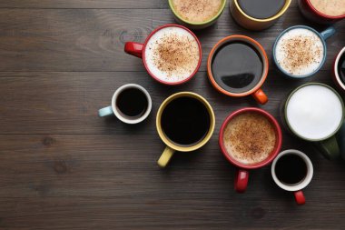 Many different cups with aromatic hot coffee on wooden table, flat lay. Space for text