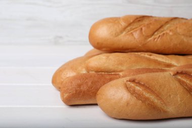 Tasty baguettes on white wooden table, closeup. Space for text