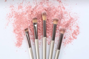 Makeup brushes and scattered eye shadow on white background, flat lay