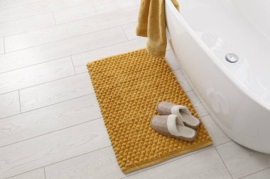 Yumuşak turuncu banyo paspası ve banyoda yerde terlikler.