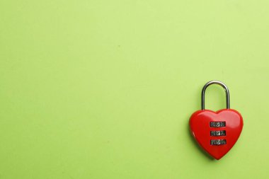 Red heart shaped combination lock on green background, top view. Space for text