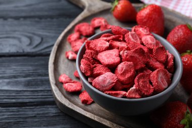 Freeze dried and fresh strawberries on black wooden table, closeup. Space for text