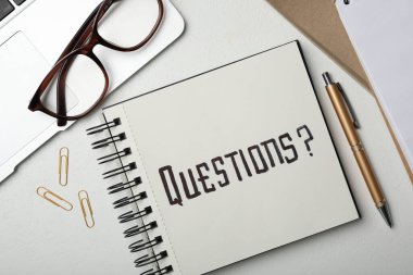 Notebook with word QUESTIONS, laptop and pen on white table, flat lay