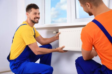 Professional plumbers installing new heating radiator in room