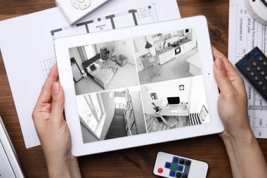 Woman monitoring CCTV cameras on tablet at wooden table, top view. Home security system