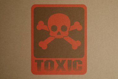 Hazard warning sign (skull-and-crossbones symbol and word TOXIC) on kraft paper, top view