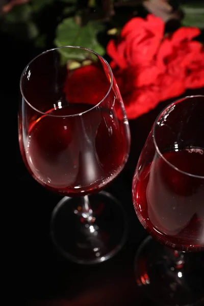 Glasses of wine and roses for romantic dinner on black table, closeup