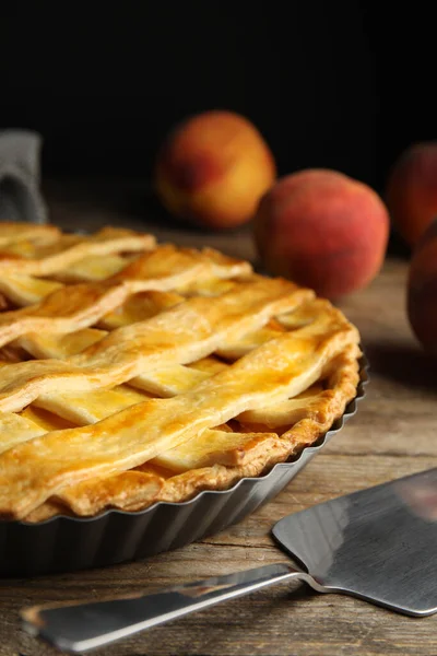 Delicious fresh peach pie and spatula on wooden table, closeup