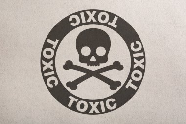 Hazard warning sign (skull-and-crossbones symbol and word TOXIC) on paper, top view