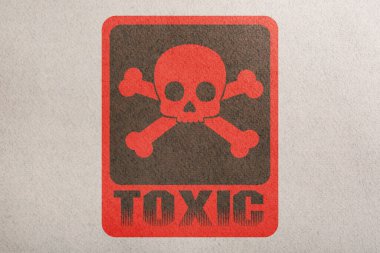 Hazard warning sign (skull-and-crossbones symbol and word TOXIC) on paper, top view
