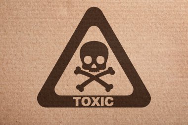 Hazard warning sign (skull-and-crossbones symbol and word TOXIC) on cardboard, top view