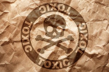 Hazard warning sign (skull-and-crossbones symbol and word TOXIC) on crumpled kraft paper, top view