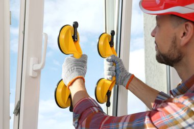 Worker using suction lifters during plastic window installation indoors