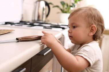 Little child touching sharp knife indoors. Dangers in kitchen