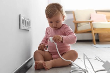 Cute baby playing with plug at home. Dangerous situation