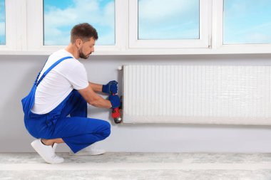 Professional plumber using adjustable wrench for installing new heating radiator in room