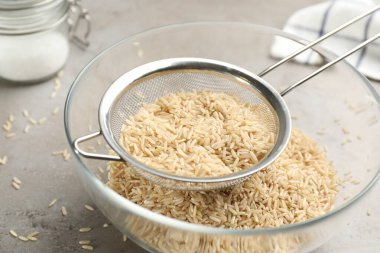 Sieve rice in bowl on grey table, closeup